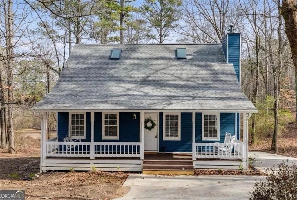 View of front facade featuring a shingled roof, a chimney, and covered porch