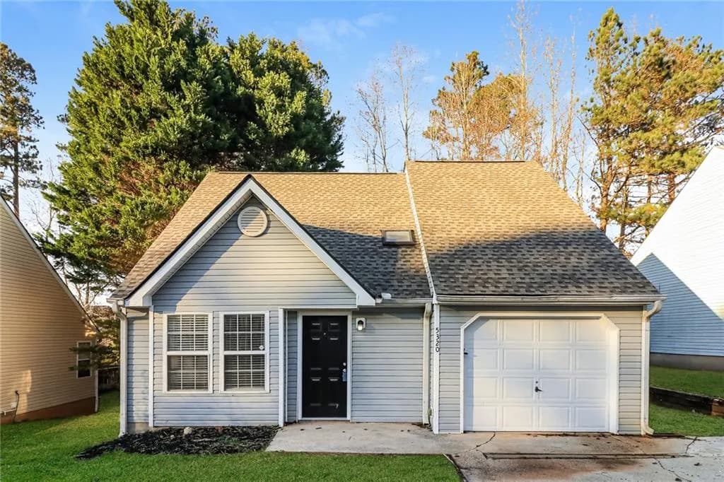 View of front facade with roof with shingles, a garage, driveway, and a front yard