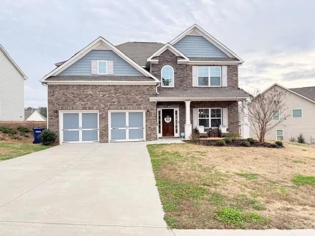 Craftsman-style home with a front lawn, driveway, a porch, and brick siding