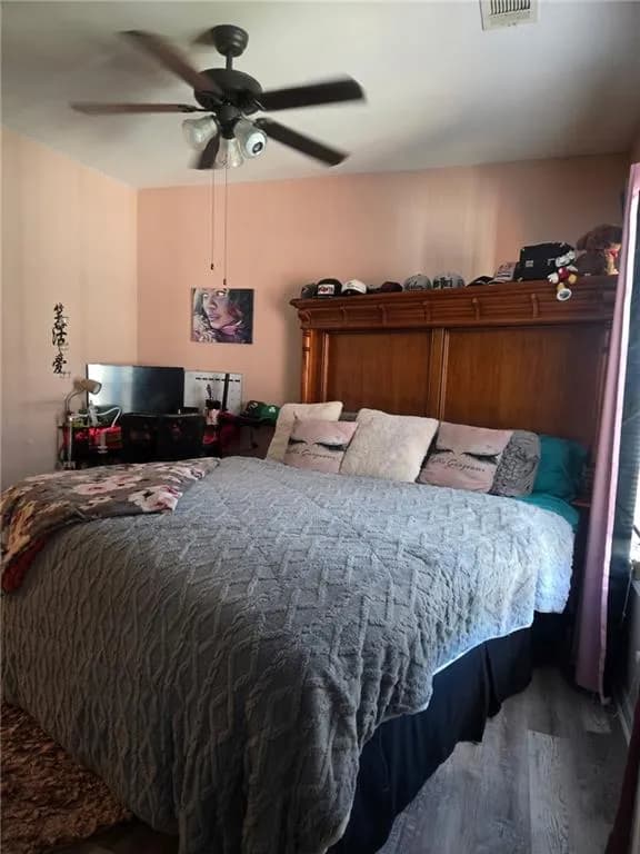 Spacious bedroom featuring an overhead ceiling fan with integrated lighting, wood-finish flooring, and a window with vertical blinds