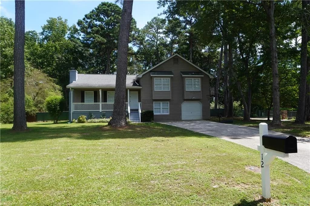 Tri-level home featuring covered porch, an attached garage, concrete driveway, a chimney, and view of wooded area