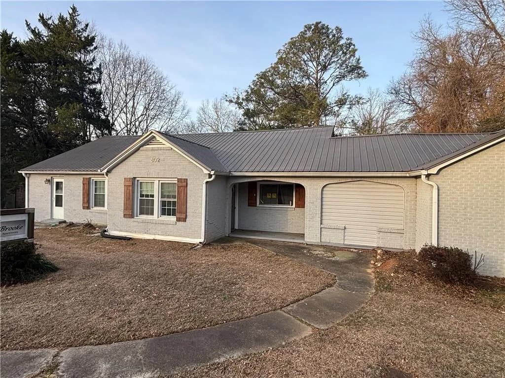 Ranch-style house featuring brick siding, a metal roof, and covered porch