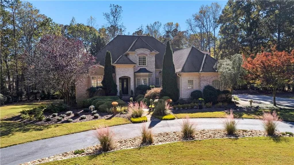 French country home with a front lawn, stone siding, brick siding, and curved driveway