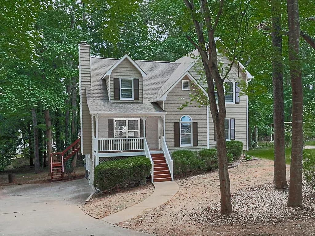 Two-story residence featuring light-colored siding, a covered front porch with white railings, and a wooded lot