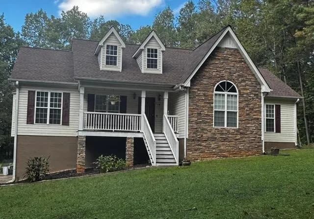 View of front of home featuring stone siding, stairs, and a front lawn