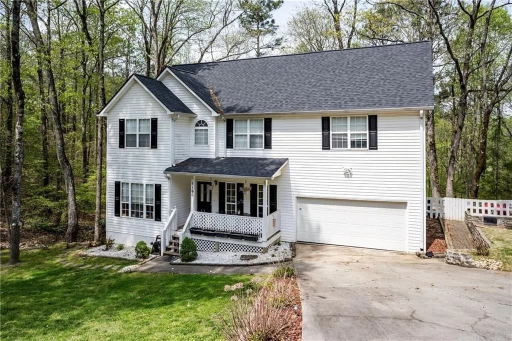 Traditional home with a porch, a garage, concrete driveway, a front yard, and a shingled roof