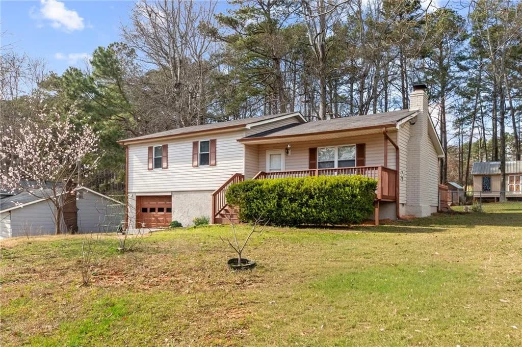 Split level home featuring a garage, a chimney, a front yard, and covered porch