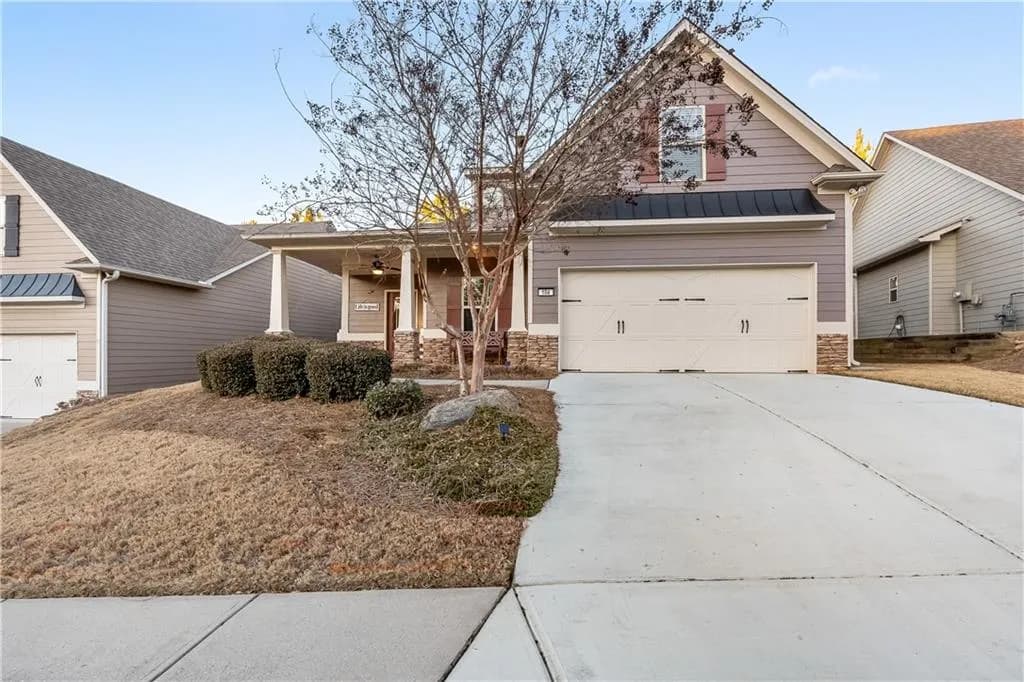 Traditional-style house with a standing seam roof, stone siding, covered porch, driveway, and an attached garage