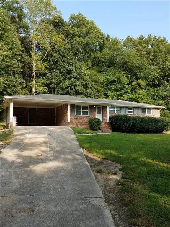 Single story home featuring a front yard, brick siding, driveway, and a carport