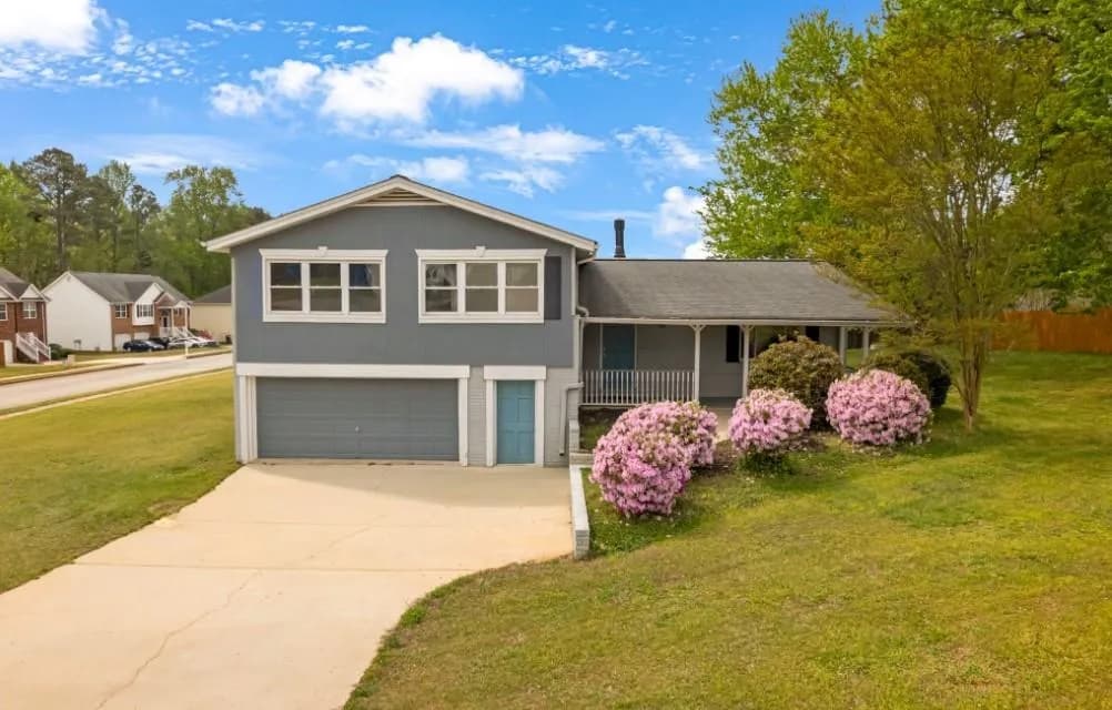 Tri-level home featuring a front lawn, an attached garage, driveway, and covered porch