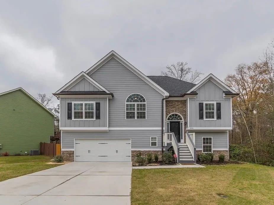 Two-story residence featuring light gray siding, dark stone accents, an arched entry door, a two-car garage, and a concrete driveway