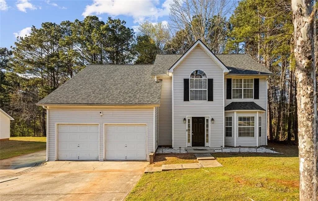 Traditional home featuring a shingled roof, concrete driveway, a front lawn, and a garage