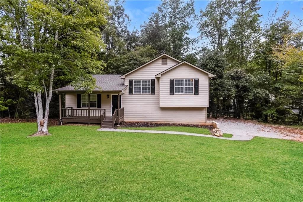 Tri-level home with a front lawn, covered porch, roof with shingles, and view of scattered trees