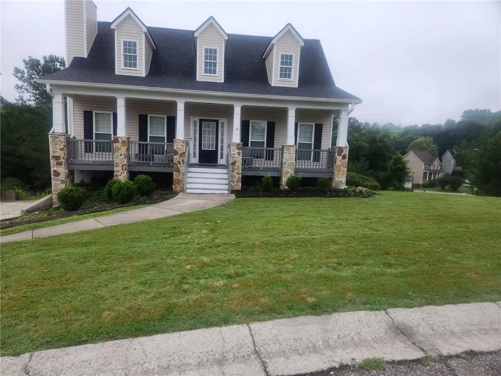 View of front of home with covered porch, a front yard, a chimney, roof with shingles, and stone siding