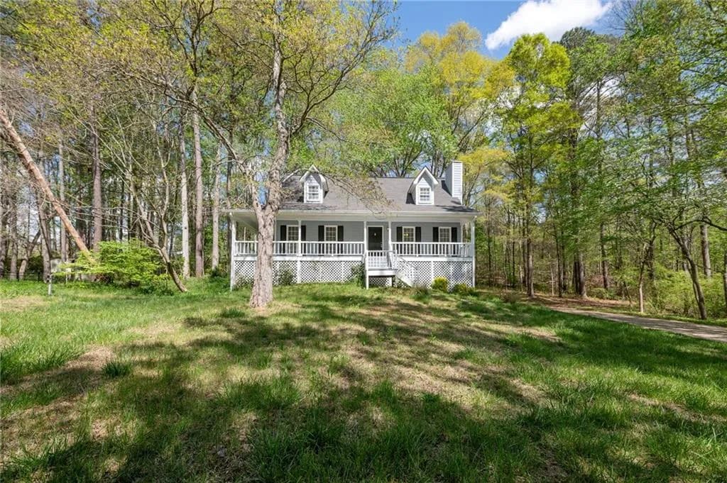 View of front facade with a front yard, covered porch, a chimney, and view of scattered trees