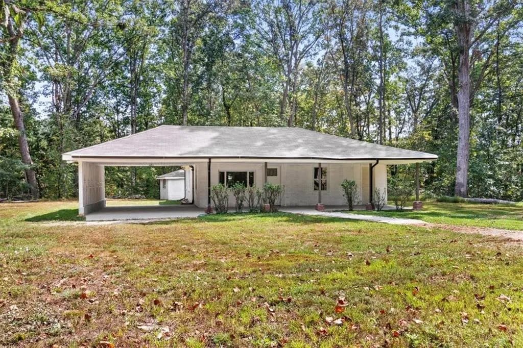 Ranch-style house with a front lawn, an attached carport, covered porch, and view of trees - private yard