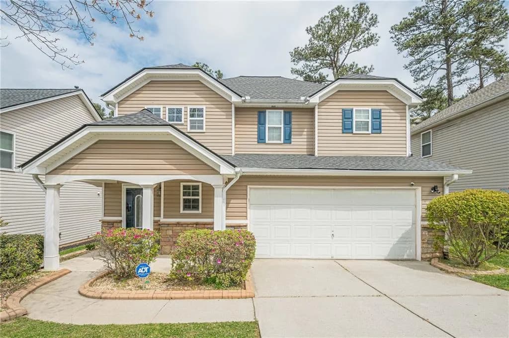 View of front of home with a porch, a shingled roof, driveway, stone siding, and an attached garage