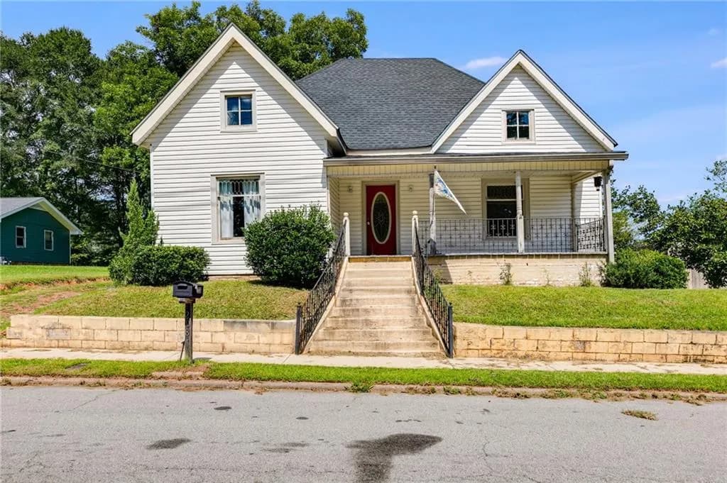 View of front of property with a porch, a front yard, roof with shingles, and stairs