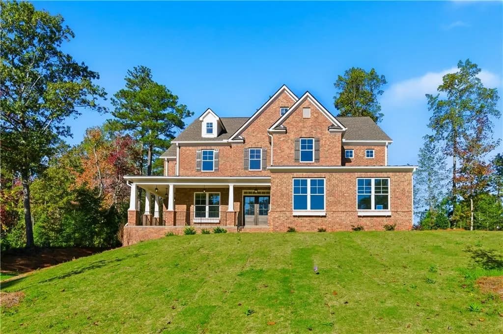 View of front of home with brick siding, covered porch, a front lawn, and french doors