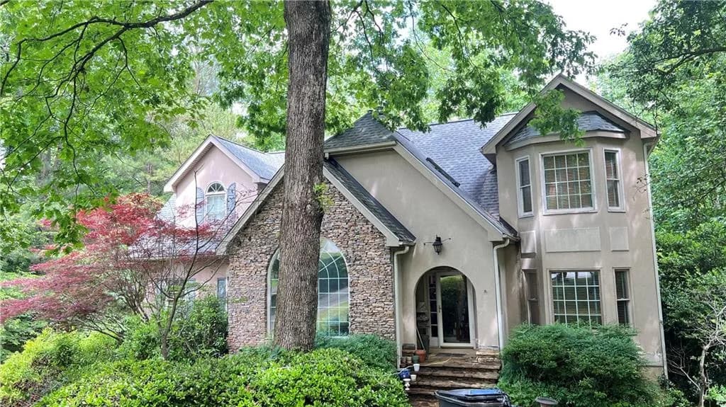 View of front of home featuring stucco siding, stone siding, and roof with shingles