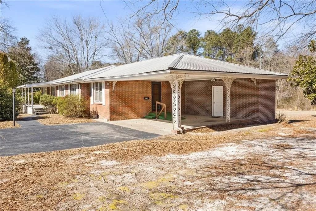 View of property exterior featuring an attached carport, brick siding, asphalt driveway, and a metal roof
