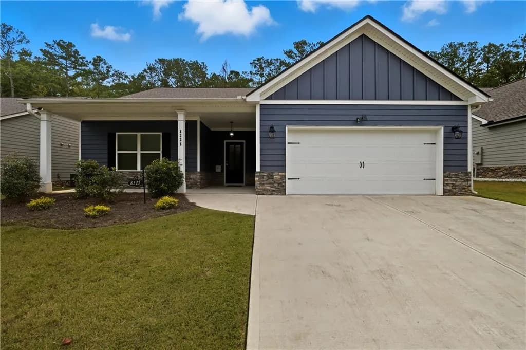 Ranch-style home featuring stone siding, board and batten siding, covered porch, driveway, and a front lawn