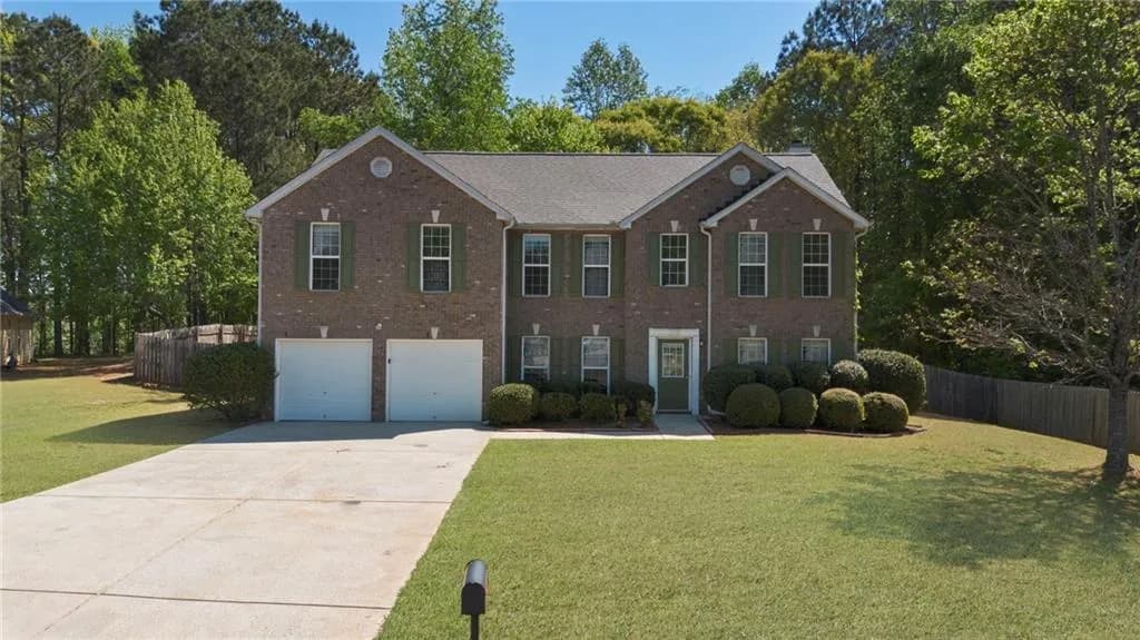 Colonial home featuring an attached garage, brick siding, driveway, and view of wooded area