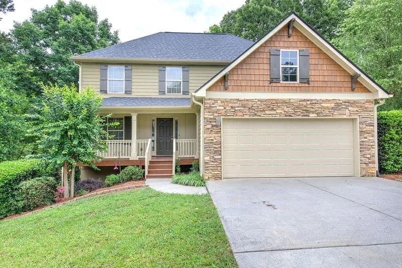 Two-story residence featuring a stone veneer garage facade, a covered front porch with railings, and a two-car garage