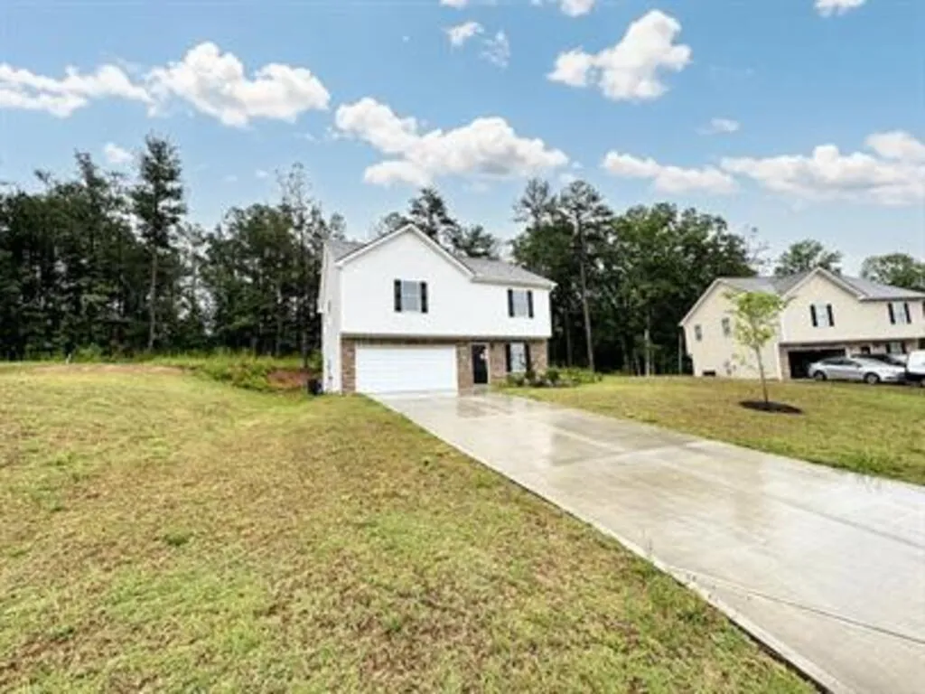 View of front facade featuring a front lawn, an attached garage, concrete driveway, and view of scattered trees