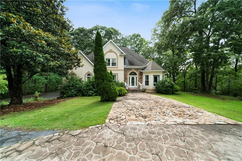 View of front facade featuring a front yard, stucco siding, a shingled roof, and view of wooded area