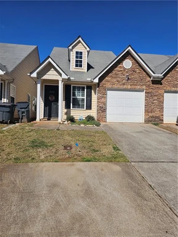 View of front of house with driveway, roof with shingles, a front lawn, an attached garage, and stone siding