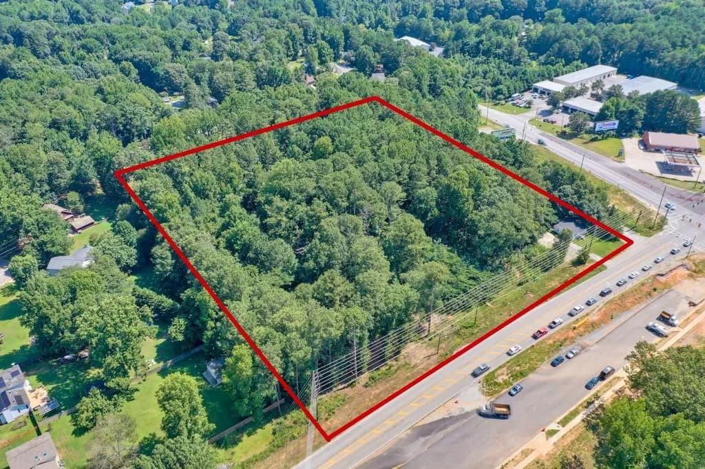 Aerial view of property and surrounding area featuring property parcel outlined and a heavily wooded area
