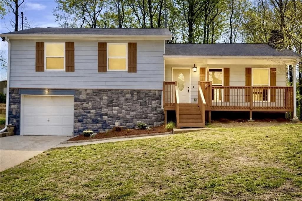 Tri-level home featuring covered porch, a garage, a front yard, and concrete driveway