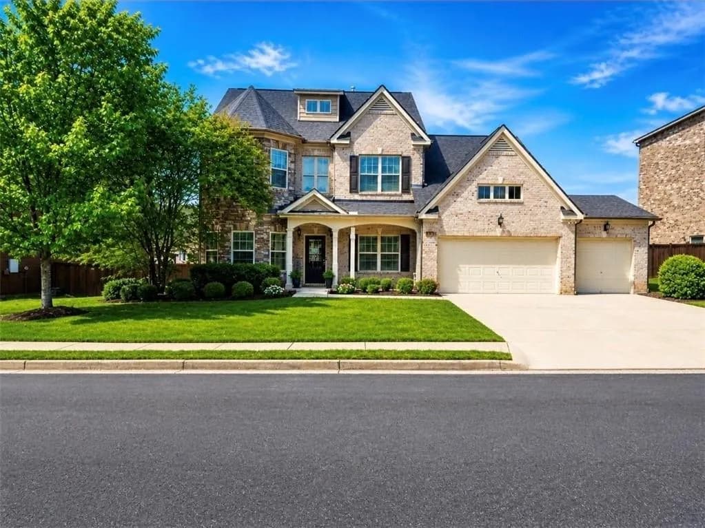 Two-story brick exterior with a multi-gabled roofline, featuring an integrated three-car garage, manicured front lawn, and mature trees
