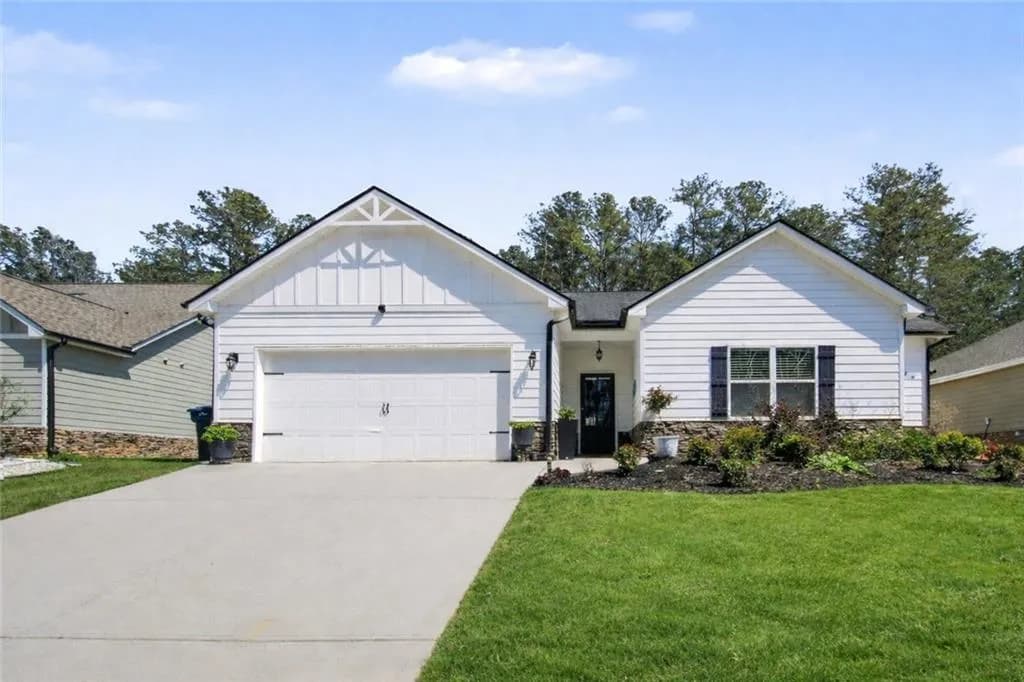 View of front of property with board and batten siding, stone siding, an attached garage, driveway, and a front yard