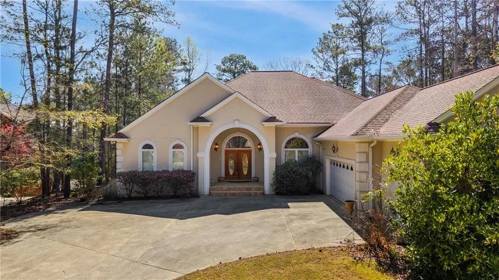 View of front of house featuring driveway, french doors, a garage, stucco siding, and roof with shingles